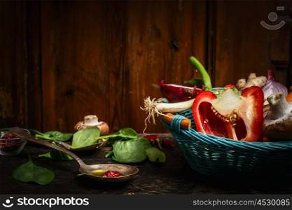 Fresh vegetables in blue basket , cooking spoon and ingredients on rustic kitchen table over wooden background. Healthy food concept.
