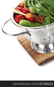 Fresh vegetables in metal colander over white