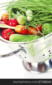 Fresh vegetables in metal colander over white