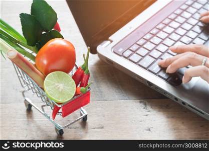 Fresh vegetables in shopping cart with woman using computer, Online shopping, Lifestyle concept