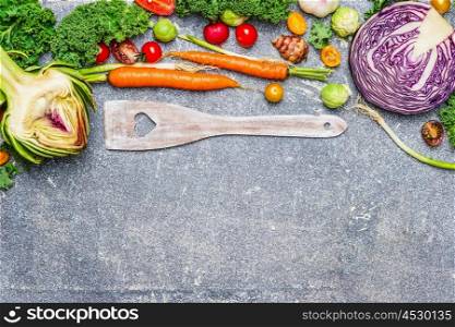 Fresh vegetables ingredients and wooden cooking spoon with heart on gray rustic background, top view. Vegetarian food, health and diet nutrition concept.