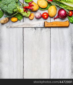 Fresh vegetables ingredients for cooking with used kitchen knife on white wooden background, top view, place for text. Vegan, diet or healthy cooking concept.