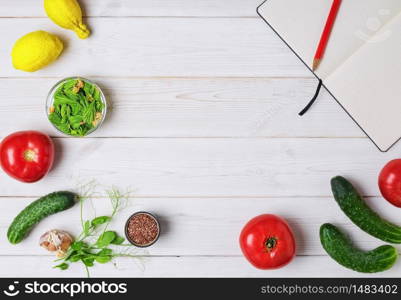 Fresh vegetables on white wooden background. Notebook for a dietary plan. Ingredients - tomatoes, cucumbers, microgreen, spruce tips, citruses. Useful foods low in carbohydrates. Copy space, flat lay. Fresh vegetables and fruits on a white wooden background, a notebook for a dietary plan. Copy space, flat lay