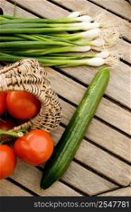 fresh vegetables tomatoes cucumber and green onion in basket over wooden table