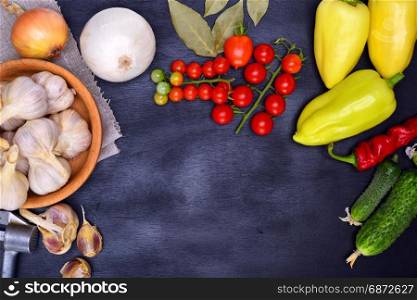 Fresh vegetables: tomatoes, cucumbers and garlic on a black background, empty space in the middle