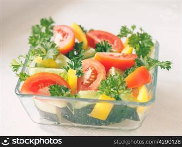 Fresh vegetables with greens in a transparent bowl on a light background