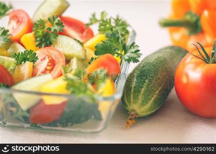 Fresh vegetables with greens in a transparent bowl on a light background