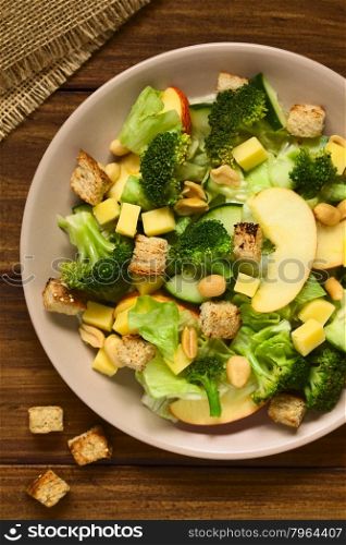 Fresh vegetarian salad with apple, lettuce, broccoli, cucumber, peanut, cheese and homemade croutons on plate, photographed overhead with natural light (Selective Focus, Focus on the upper pieces on the salad)
