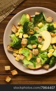 Fresh vegetarian salad with apple, lettuce, broccoli, cucumber, peanut, cheese and homemade croutons on plate, photographed overhead with natural light (Selective Focus, Focus on the upper pieces on the salad)