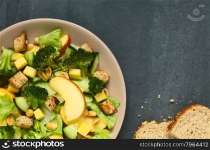 Fresh vegetarian salad with apple, lettuce, broccoli, cucumber, peanut, cheese and homemade croutons on plate, photographed overhead with natural light (Selective Focus, Focus on the top pieces on the salad)