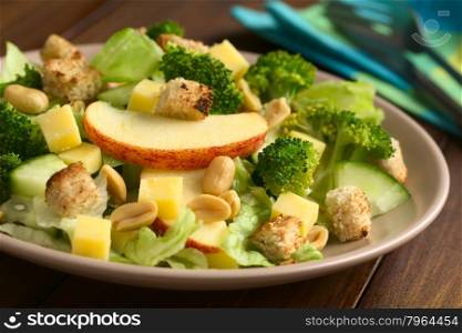 Fresh vegetarian salad with apple, lettuce, broccoli, cucumber, peanut, cheese and homemade croutons on plate, photographed with natural light (Selective Focus, Focus on the front of the apple slice)