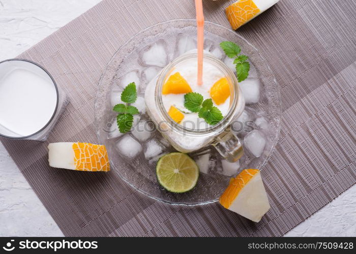 fresh vegetarian tropical melon cocktail with coconut milk and mango. served in transporant cup with ice, fresh melon, mango, lime, melissa and coconut milk on grey napkin. close up
