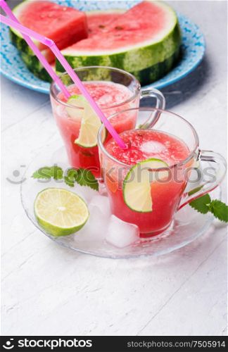 fresh vegetarian watermelon cocktail in transporant cups on white table with fresh watermelon, lime, melissa. close up