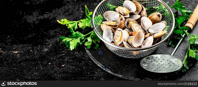 Fresh vongole in a colander on a stone board with parsley. On a black background. High quality photo. Fresh vongole in a colander on a stone board with parsley.