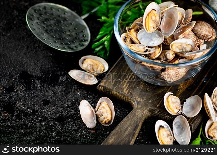 Fresh vongole in the bowl on a cutting board with parsley. On a black background. High quality photo. Fresh vongole in the bowl on a cutting board with parsley.