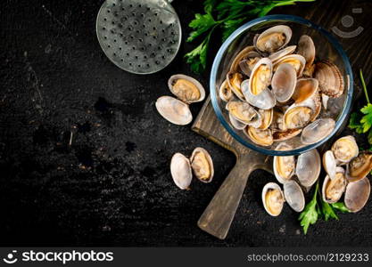 Fresh vongole in the bowl on a cutting board with parsley. On a black background. High quality photo. Fresh vongole in the bowl on a cutting board with parsley.