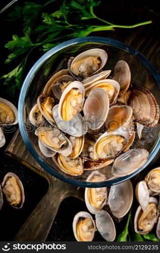 Fresh vongole in the bowl on a cutting board with parsley. On a black background. High quality photo. Fresh vongole in the bowl on a cutting board with parsley.