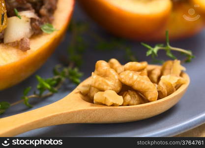 Fresh walnut pieces on wooden spoon with fresh thyme and baked apple on blue plate (Selective Focus, Focus on the front of the walnut pieces on the top)