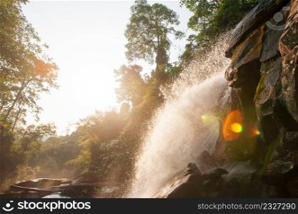 Fresh waterfall in morning light, fantastic lens flare with bright rim light. Pure nature water in tropical forest in summer season, Chiang Mai, North Thailand. Warm tone.
