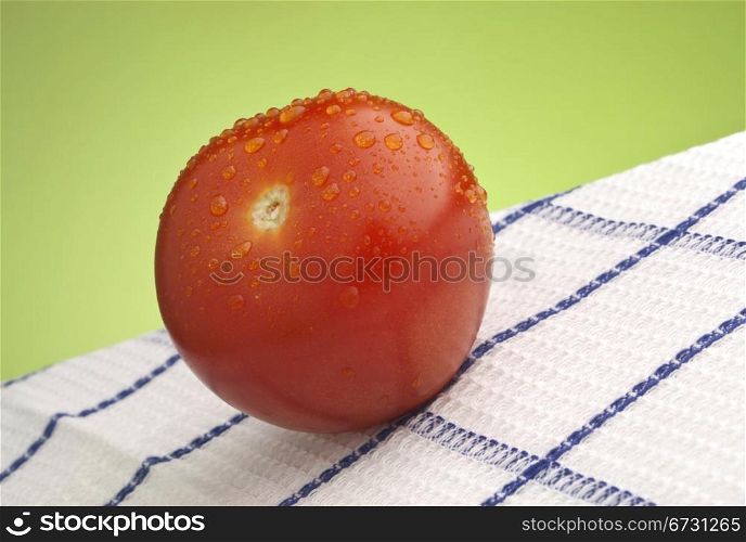 Fresh wet ripe red tomato on white and blue tablecloth against green background.