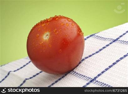 Fresh wet ripe red tomato on white and blue tablecloth against green background.