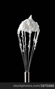 Fresh whipped egg whites on with a metal whisk on a black background with copy space. Cooking concept. A metal whisk with beaten egg whites, represented by a black background with copy space. Ingredient for dessert