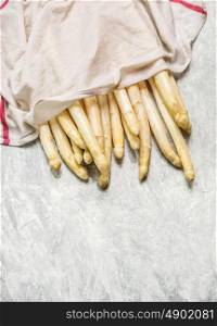 fresh white asparagus with wet kitchen towel on light wooden background, top view, place for text