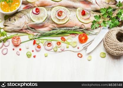 Fresh whole fish with chopped ingredients for tasty cooking on white rustic background.