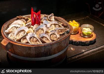 Fresh whole marine Fine de claire oysters in oak wood bucket with lime and lemon - dark tone food image