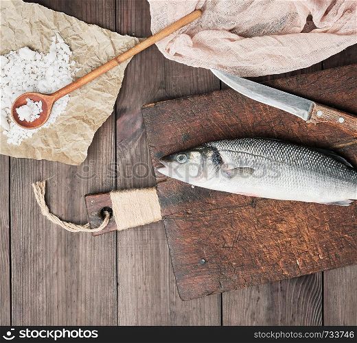 fresh whole sea bass fish and knife on brown cutting board , top view