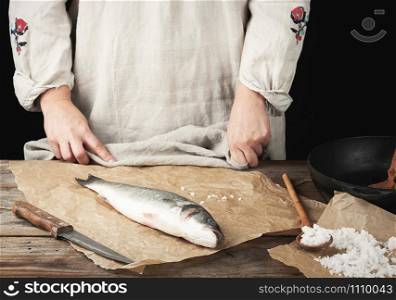 fresh whole sea bass fish lies on the table, cooking process, dark background