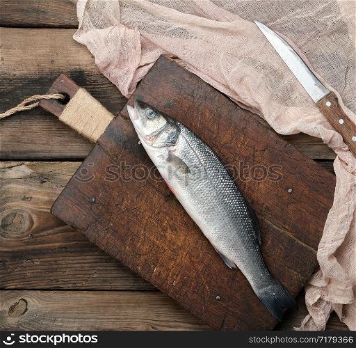 fresh whole sea bass fish on brown cutting board , top view