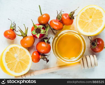 Fresh yellow lemon, jug of honey and red berries on a white wooden table. Top view, close-up, isolated. Concept of preventing colds. Fresh yellow lemon, jug of honey and red berries