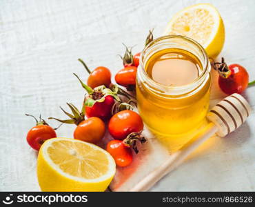 Fresh yellow lemon, jug of honey and red berries on a white wooden table. Top view, close-up, isolated. Concept of preventing colds. Fresh yellow lemon, jug of honey and red berries
