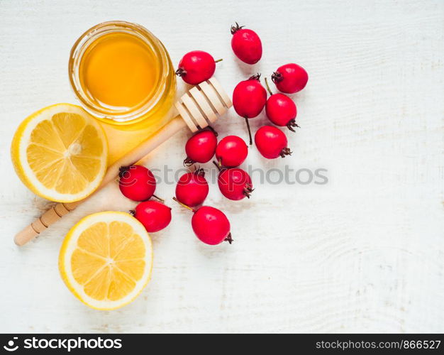 Fresh yellow lemon, jug of honey and red berries on a white wooden table. Top view, close-up, isolated. Concept of preventing colds. Fresh yellow lemon, jug of honey and red berries