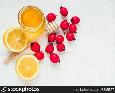 Fresh yellow lemon, jug of honey and red berries on a white wooden table. Top view, close-up, isolated. Concept of preventing colds. Fresh yellow lemon, jug of honey and red berries