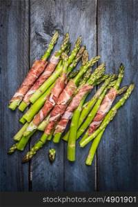 Fresh Young asparagus wrapped in prosciutto meat on rustic blue wooden background, top view