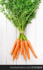 Fresh young carrots with green tops on a white rustic wooden table. Young rustic carrots on white boards