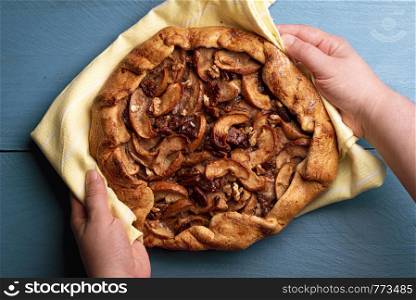 Freshly baked apple pie with pecan nuts. Rustic apple pie with a delicious crust above view in a woman's hands