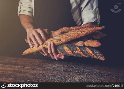 Freshly baked baguettes hold a man’s hands against a background of a wooden table, tonned photo. Men’s hands hold baguettes