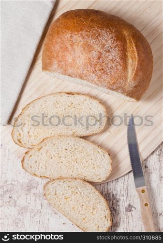 Freshly baked bread loaf with pieces on wood boardon wooden board with kitchen towel and knife