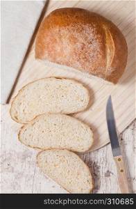 Freshly baked bread loaf with pieces on wood boardon wooden board with kitchen towel and knife