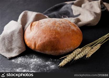 Freshly baked bread with flour and kitchen towel on black background