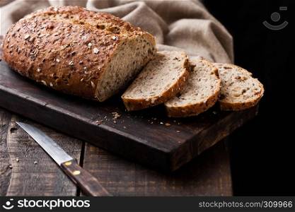 Freshly baked bread with kitchen towel and knife on dark wooden board