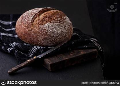 Freshly baked bread with kitchen towel and knife on dark wooden board