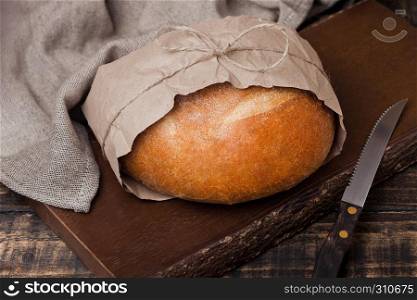 Freshly baked bread with kitchen towel and knife on wooden chopping board