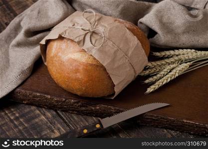 Freshly baked bread with kitchen towel and knife on wooden chopping board