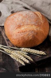 Freshly baked bread with kitchen towel and wheat on dark wooden board