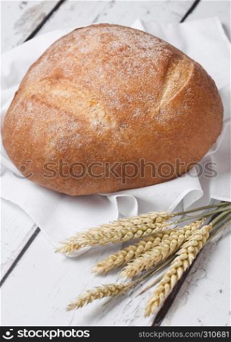 Freshly baked bread with kitchen towel and wheat on white wooden board