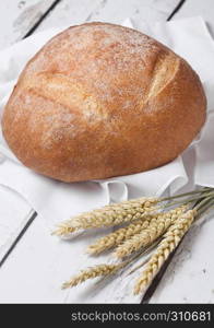 Freshly baked bread with kitchen towel and wheat on white wooden board